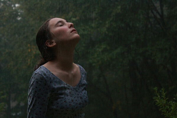 Kobieta wystawia twarz w stronę spadających kropel deszczu