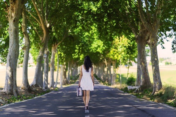 Kobieta idąca drogą pośród drzew