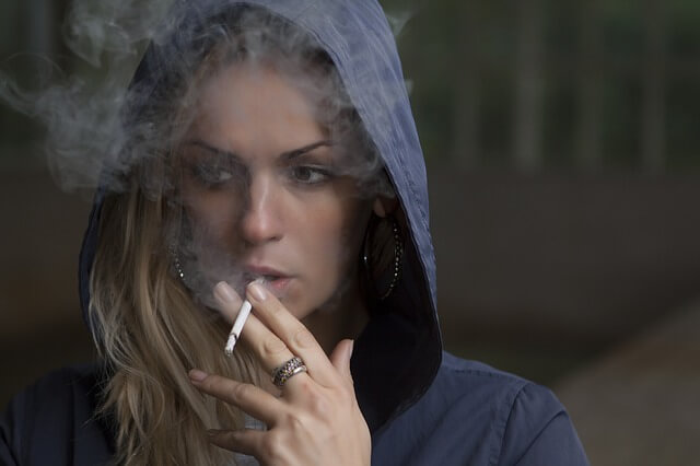 Dziewczyna w bluzie z kapturem pali papierosa