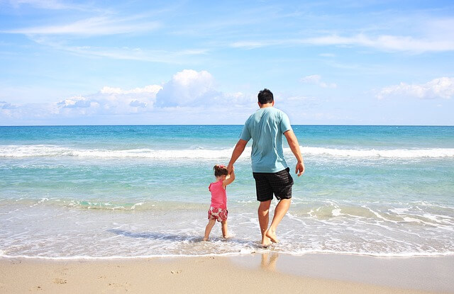 Ojciec z dzieckiem spacerują nad brzegiem morza